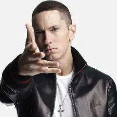 Eminem w czarnej kurtce i białej koszulce, gestykuluje ręką.