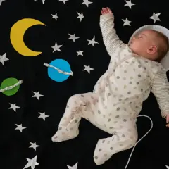 Śpiące dziecko w piżamce z kropkami, jak mały astronauta, wśród gwiazd i planet. Ach śpij kochanie tekst pasuje idealnie.