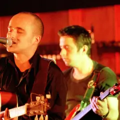 Wokalista z gitarą śpiewa do mikrofonu, i nawet kiedy będę sam, czuje wsparcie kolegi z zespołu.