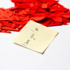 Serce z czerwonych skrawków papieru, a na nim karteczka z napisem "I love you!". Kocham Cię po polsku.