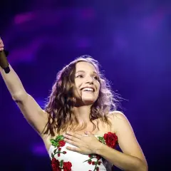 Sanah śpiewa "Bujda" na koncercie, trzymając złoty mikrofon i dotykając serca.