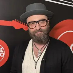 Mężczyzna w kapeluszu i okularach, z brodą, na tle logo Rock Radia. Widać napis "perfect wszystko ma swój czas tekst".
