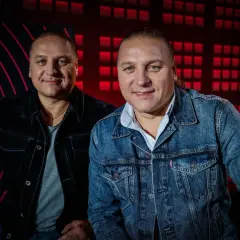 Dwóch mężczyzn w dżinsowych kurtkach, z charakterystycznym kucykiem. Tło to czerwone, geometryczne wzory, przypominające ściernisko tekst.