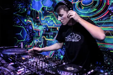 DJ w słuchawkach miksuje muzykę na tle psychodelicznej, neonowej grafiki.