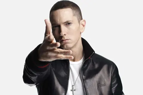 Eminem w czarnej kurtce i białej koszulce, gestykuluje ręką.