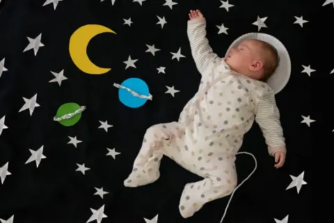 Śpiące dziecko w piżamce z kropkami, jak mały astronauta, wśród gwiazd i planet. Ach śpij kochanie tekst pasuje idealnie.