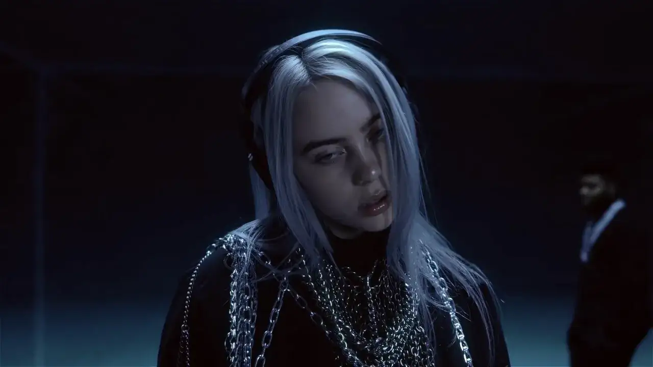 Billie Eilish w słuchawkach, z łańcuchami na szyi, w mrocznym klimacie. Tekst 