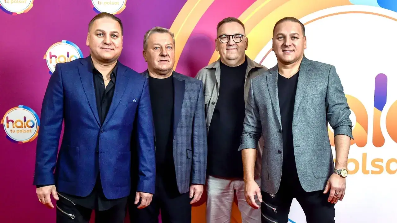 Czterech mężczyzn w eleganckich marynarkach pozuje na tle logo