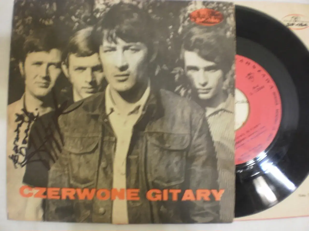 Okładka płyty Czerwone Gitary z wizerunkiem zespołu. W tle widać fragment czarnej płyty winylowej.