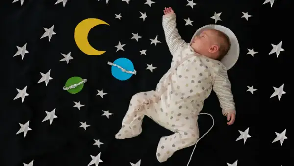 Śpiące dziecko w piżamce z kropkami, jak mały astronauta, wśród gwiazd i planet. Ach śpij kochanie tekst pasuje idealnie.